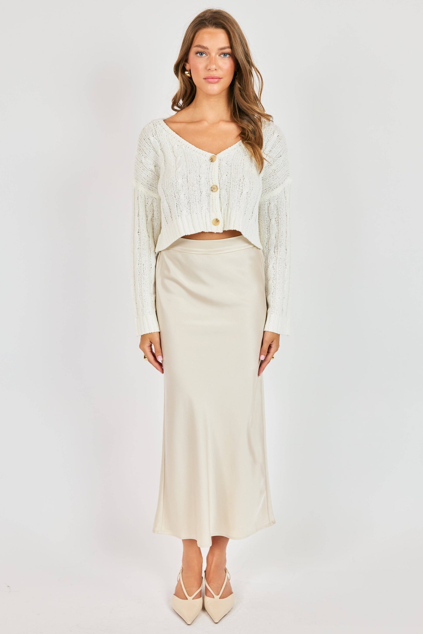 Woman wearing a white cardigan and beige skirt on a white background