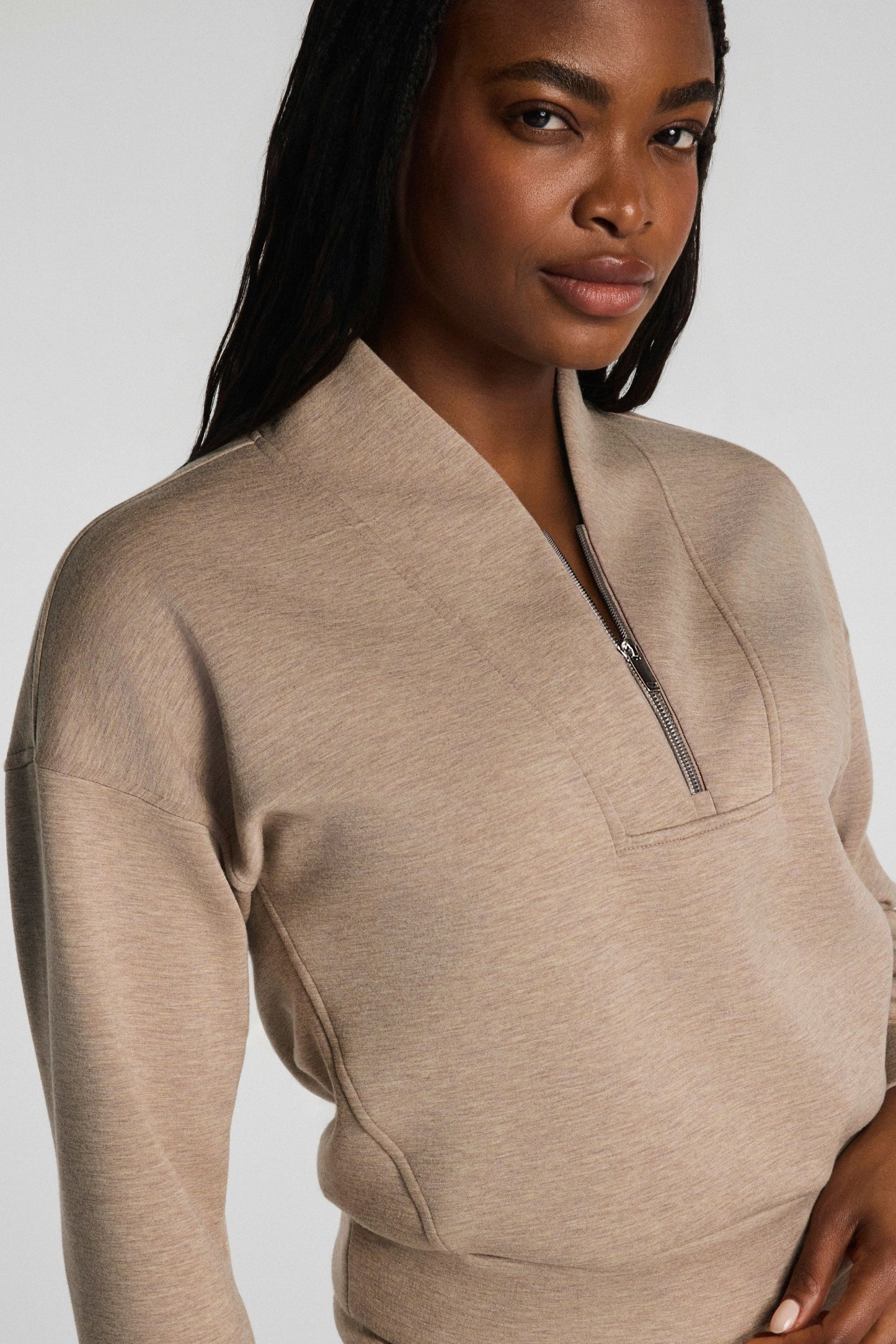Woman wearing a beige zip-up sweatshirt against a plain background