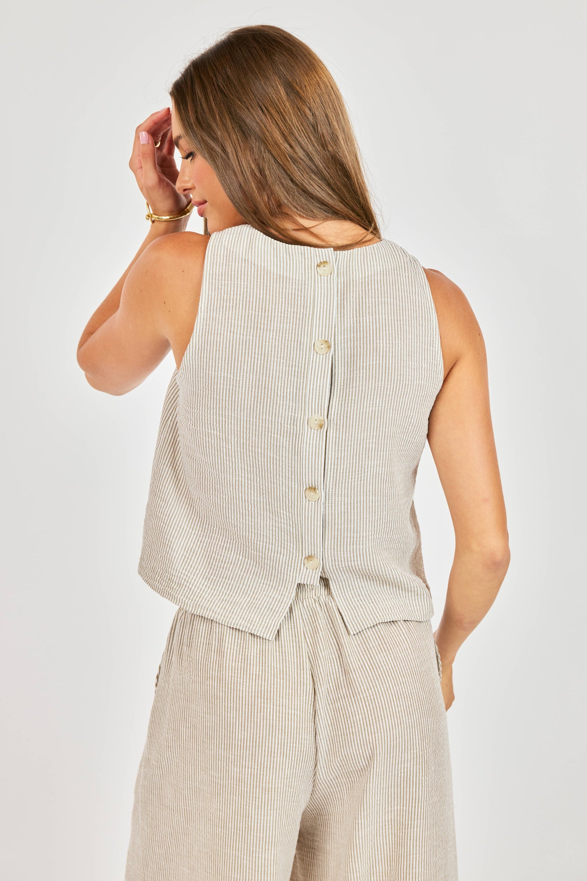 Woman wearing a beige sleeveless top and pants against a white background
