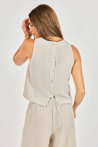 Woman wearing a beige sleeveless top and pants against a white background