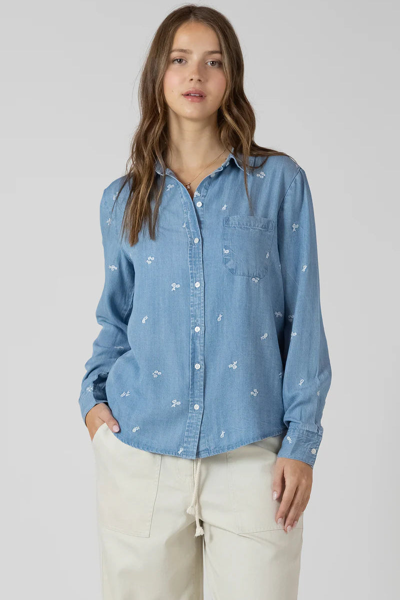 Woman wearing a blue denim shirt with white floral patterns on a plain background