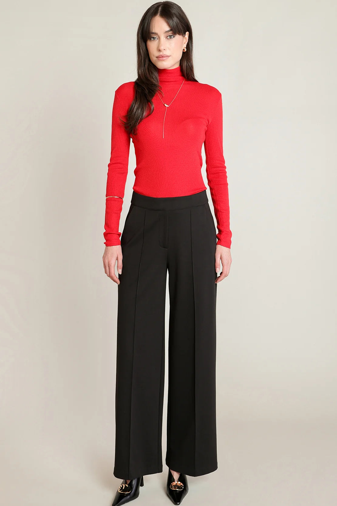 Woman wearing a red top and black pants on a beige background