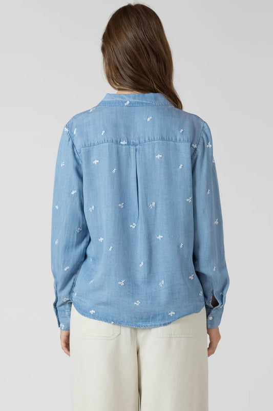 Woman wearing a light blue denim shirt with white patterns on a plain background