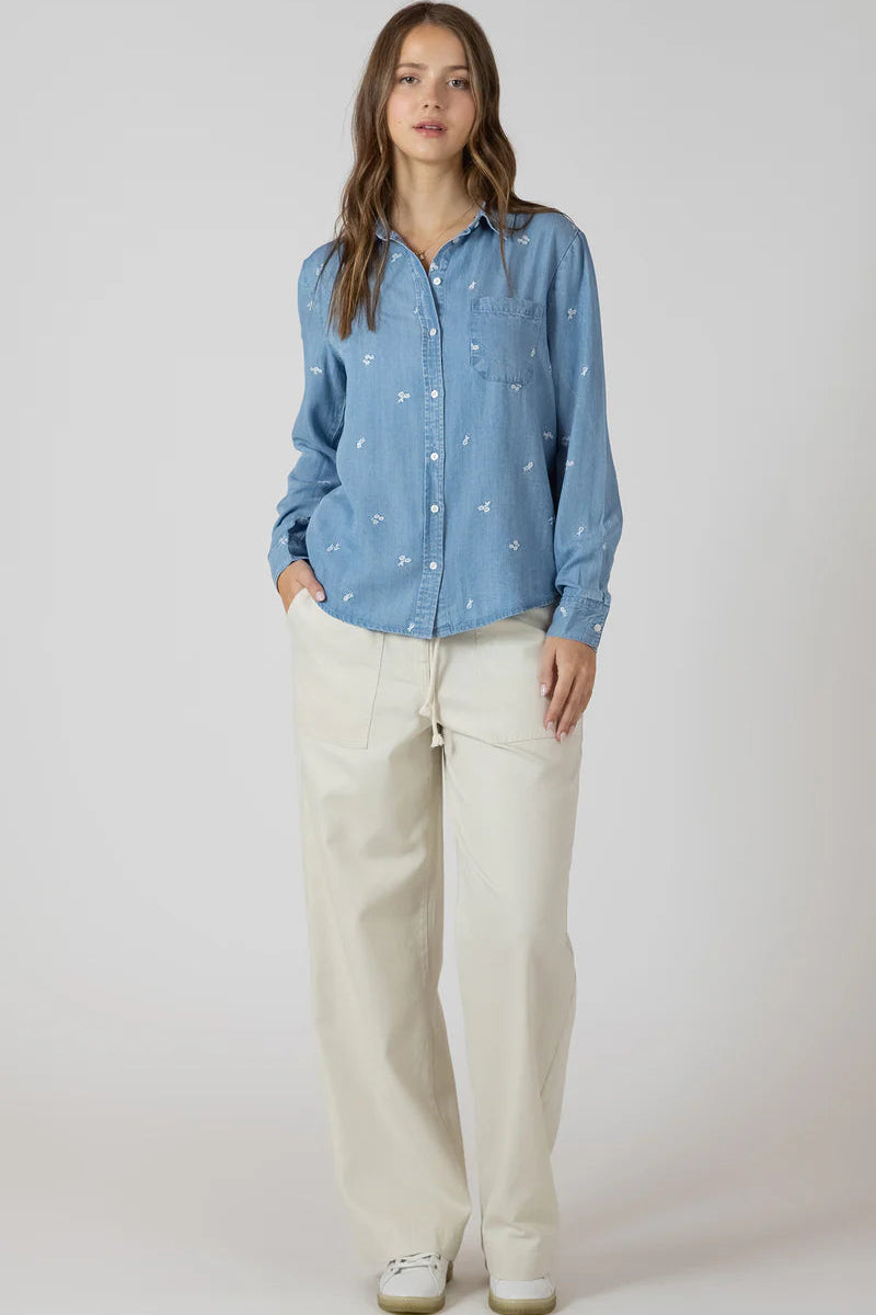 Woman wearing a blue patterned shirt and beige pants on a white background