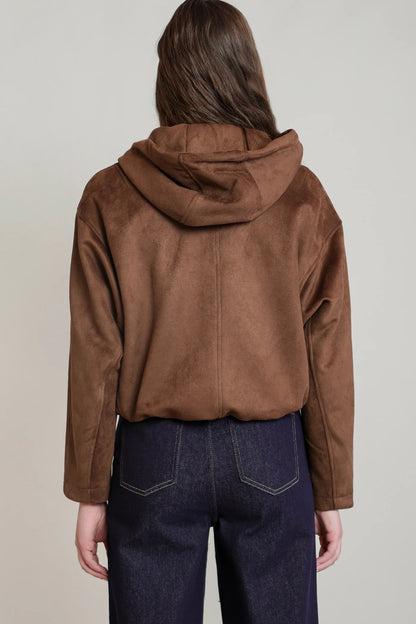 A person shown from the back wearing a brown hooded jacket with a suede-like finish and dark blue jeans, against a plain light gray studio background.