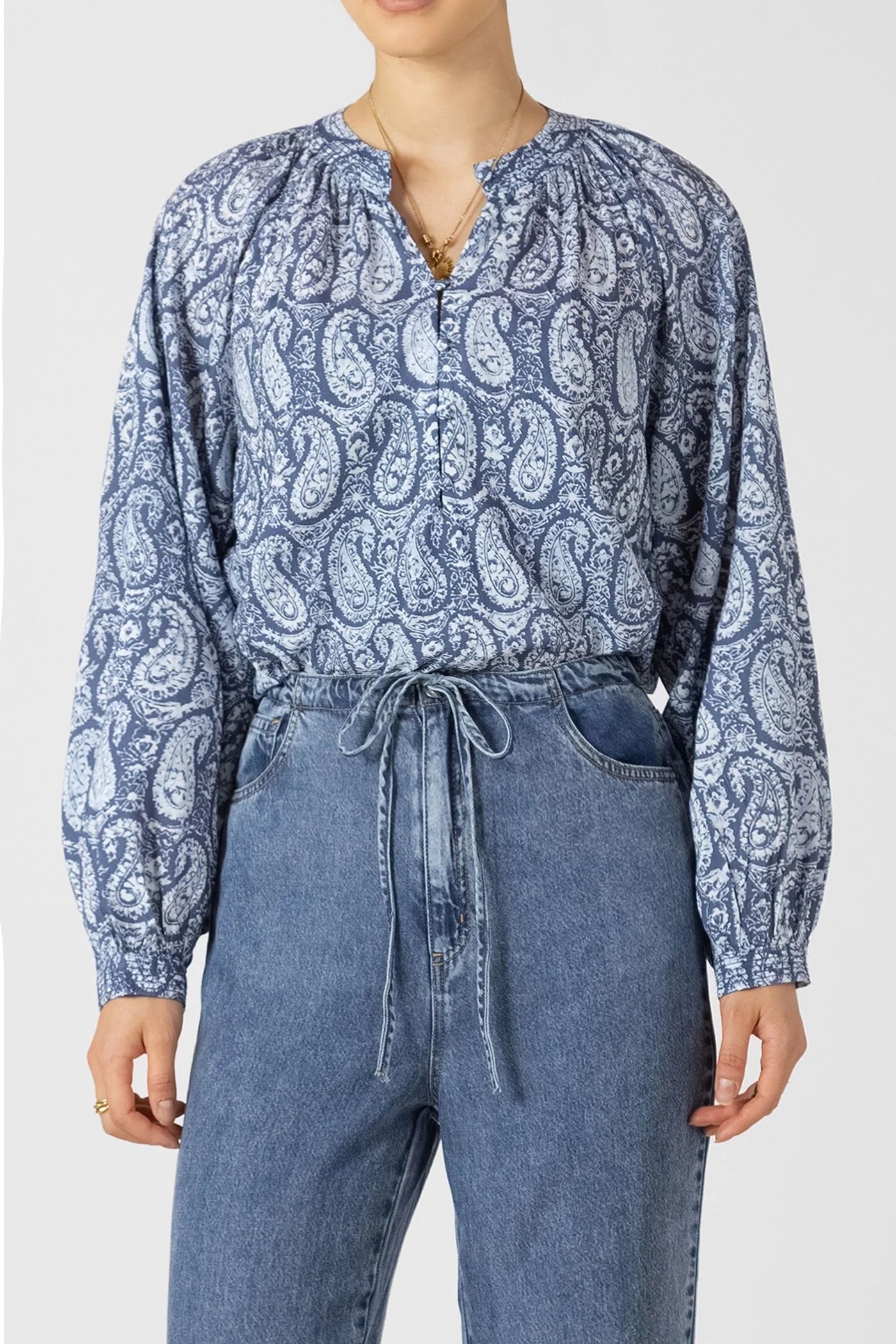 Person wearing a blue paisley blouse and jeans on a white background