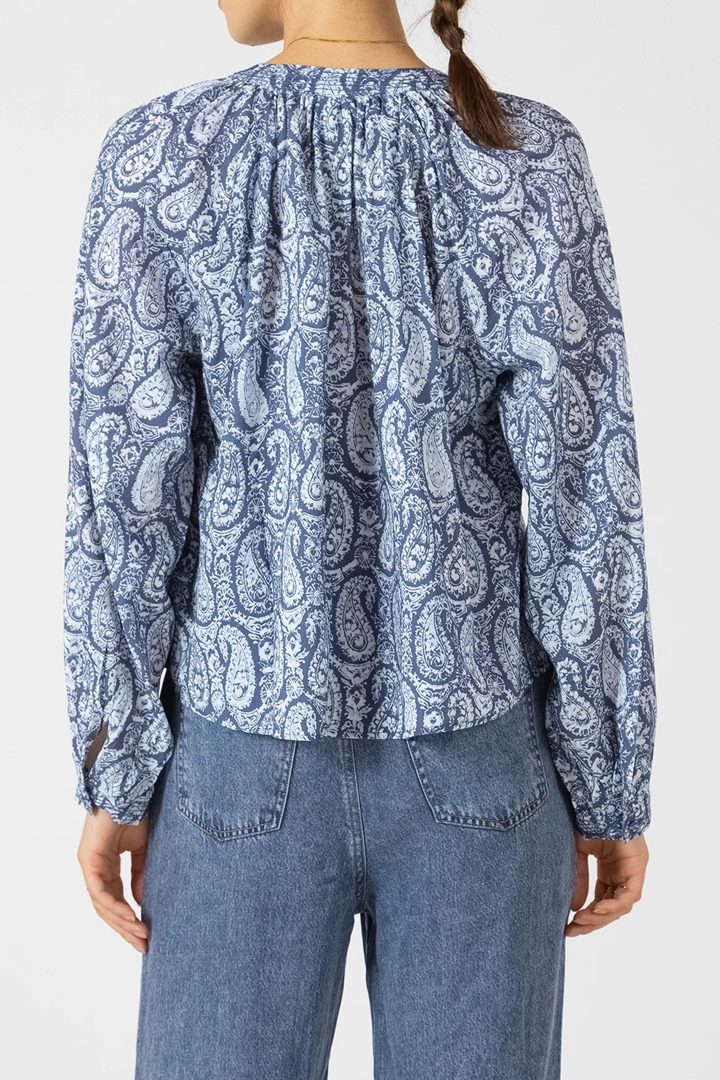 Person wearing a blue paisley patterned blouse and jeans on a white background