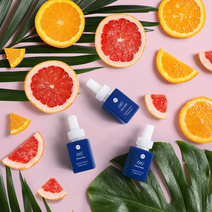 Three blue skincare bottles with droppers on a pink background with orange and grapefruit slices.