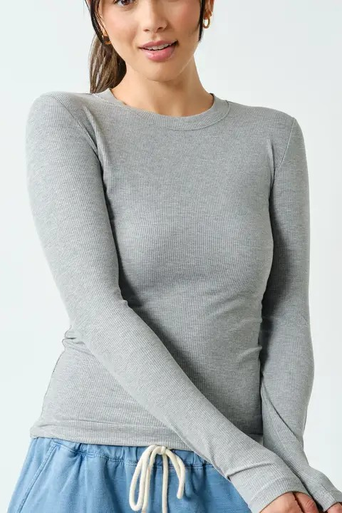 A woman wearing a fitted long-sleeve crewneck top in heather gray, paired with light blue drawstring shorts, against a clean white studio background.