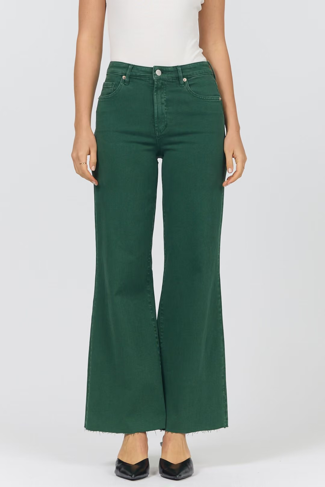 A model wearing a pair of dark green wide-leg cropped jeans with a frayed hem, paired with a white top and black pointed-toe heels, shown against a light gray studio background.