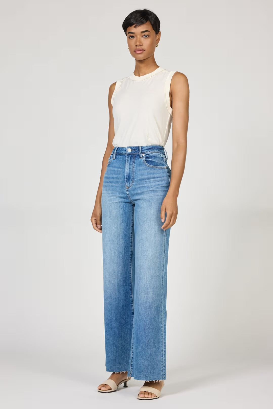 Woman wearing a white sleeveless top and light blue jeans on a white background