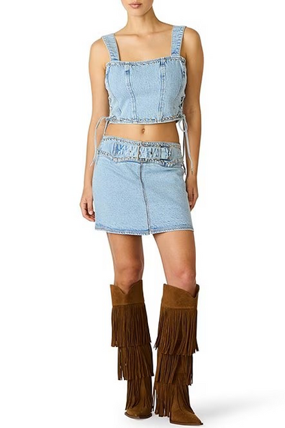 Person wearing a denim outfit with a crop top and shorts, paired with brown fringed boots on a white background.