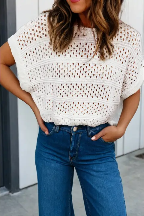 Woman wearing a white crochet top and blue jeans against a neutral background